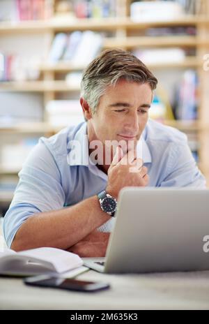 HES ist tief in das World Wide Web vertieft. Ein gut aussehender, reifer Mann, der mit einem Laptop auf dem Boden seines Wohnzimmers liegt. Stockfoto