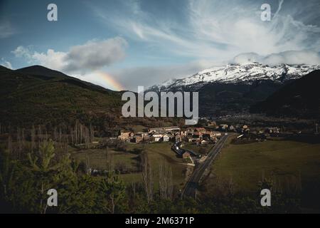 Malerische Landschaft mit einem kleinen Dorf mit typischen Wohnhäusern auf einer Wiese, umgeben von grünen und schneebedeckten Bergen und Wolkenblau Stockfoto