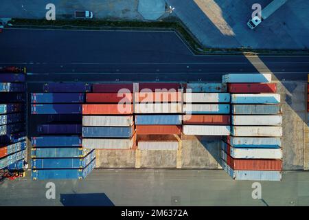 Versandcontainer im Terminal, Entladen von Containern im Lager auf der Eisenbahnplattform mit Kränen und Gabelstaplern, Luftaufnahme Stockfoto