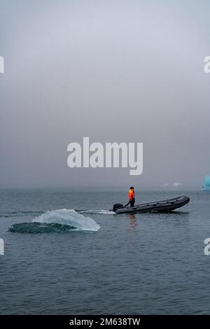 Seitenansicht einer anonymen Person, die auf einem Motorboot steht und an einem nebligen Tag in der Nähe des Eisbergs in Island in kaltem Meerwasser segelt Stockfoto