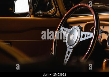 Lenkrad aus Holz und Stahl in einem luxuriösen Cabriolet mit Innenraum aus beigefarbenem Leder in einer Garage Stockfoto