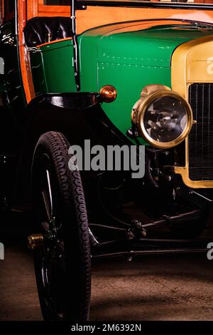 Runder Scheinwerfer und große Räder aus altgrün-gelbem Tourauto mit schwarzen Ledersitzen in der Garage Stockfoto