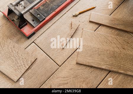 Draufsicht auf staubiges rotes Fliesenschneider, das während der Renovierung neben Stücken und Bleistift auf dem Boden platziert wurde Stockfoto