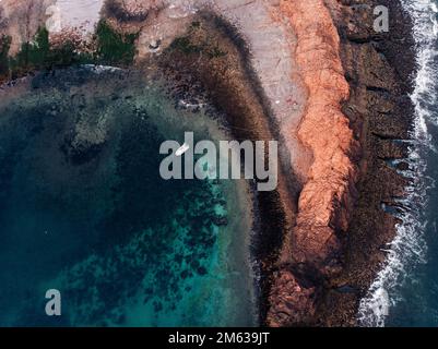 Von oben malerische Landschaft des weißen Bootes, das auf klarem azurblauem Meerwasser in der Nähe des steinigen Vorgewendes schwimmt Stockfoto