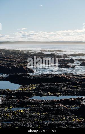 Malerischer Blick auf raue Felsformationen mit unebenen Steinen und Pfützen in der Nähe des blauen Meeres unter blauem Himmel in Cabo Raso Stockfoto
