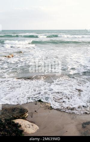 Schäumende Wellen am nassen Sandstrand, bedeckt mit Seetang an stürmischen Tagen in Sizilien, Italien Stockfoto