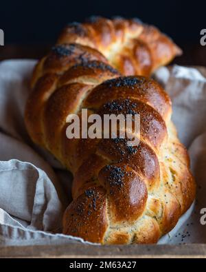 Serviert werden goldbraune Brotgeflechte Challah mit Mohnsamen auf weißer Serviette in einer Holzbox Stockfoto