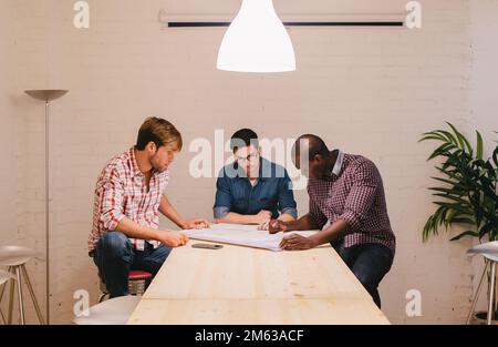 Architekten und Ingenieure, die im Büro arbeiten, sitzen auf einem großen Tisch Stockfoto