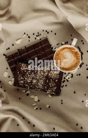 Draufsicht auf eine Tasse frischen Kaffees, die auf einer Tischdecke in der Nähe von Schokoriegeln mit Nüssen platziert wurde Stockfoto