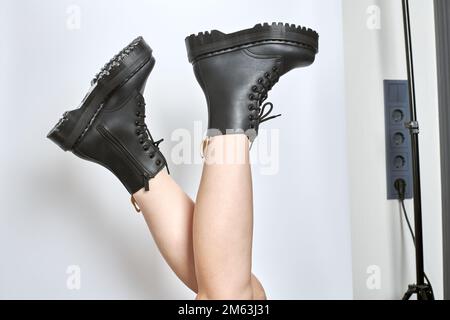 Frauenbeine in schwarzen Kampfstiefeln auf einer Plattform mit hohem Absatz und umgedrehten Stollensohlen auf isoliertem weißem Hintergrund. Weibliche Beine tragen militärausrüstung Stockfoto