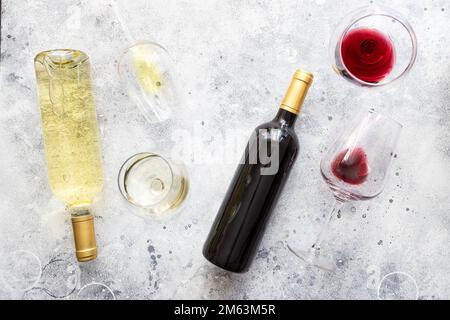 Rot- und Weißwein in Gläsern und Flaschen auf grauem Betonhintergrund. Konzept der Weinverkostung Stockfoto