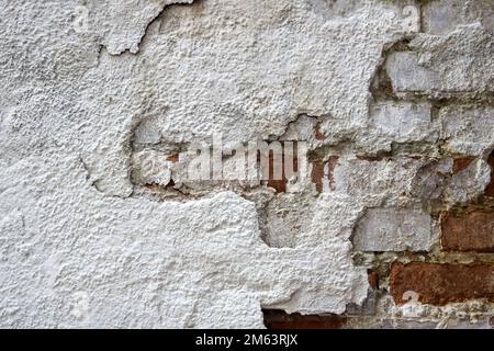 Textur alter Ziegelmauern mit zusammengefallenem Putz. Hintergrund einer schäbigen Gebäudefläche. Zerstörte Beton- und Ziegelwand mit heruntergefallenem Putz. Weathe Stockfoto