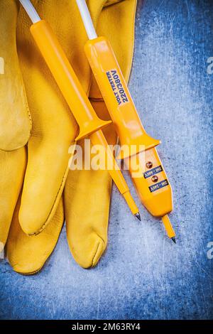 Gelbe Schutzhandschuhe für elektrische Prüfgeräte auf metallischem Hintergrund. Stockfoto