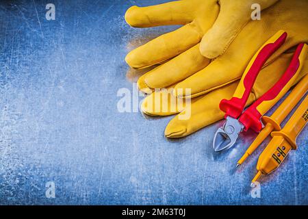 Gelbe Schutzhandschuhe für elektrische Prüfgeräte Schneidzange auf metallischem Hintergrund. Stockfoto