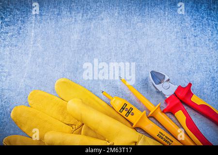 Gelbe Sicherheitshandschuhe für elektrische Tester, rote Knipser auf metallischem Hintergrund. Stockfoto