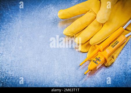 Gelbe Sicherheitshandschuhe für elektrische Tester auf zerkratztem metallischem Hintergrund Konzept der Elektrizität. Stockfoto