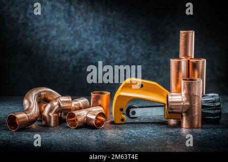 Gelber Rohrabschneider und Kupferrohr mit Anschlüssen auf dunklem Hintergrund Stockfoto