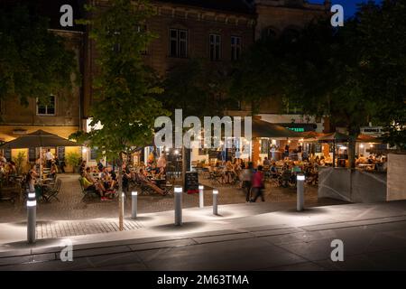 Ljubljana, Slowenien - 14. Juli 2022: Gruppe von Personen an Restauranttischen, die das Abendessen im Sommer am Flussufer des Petkovskovo Nabrezje bei Nacht genießen, Stockfoto