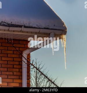 Eiszapfen auf dem Sims eines privaten Hauses spielen in den Strahlen der aufgehenden Sonne. Stockfoto