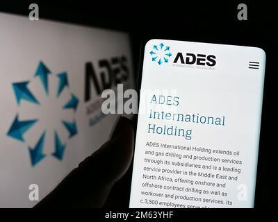 Person, die ein Mobiltelefon mit der Website des ägyptischen Unternehmens ADES International Holding auf dem Bildschirm vor dem Logo hält. Konzentrieren Sie sich auf die Mitte des Telefondisplays. Stockfoto