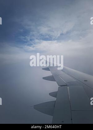 Flugzeugflug durch die dichten nebligen Wolken, vertikaler Schuss. Flugzeugflügel durch das Fenster gesehen Stockfoto