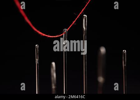 Roter Faden durch Nadeln auf schwarzem Hintergrund. Stockfoto