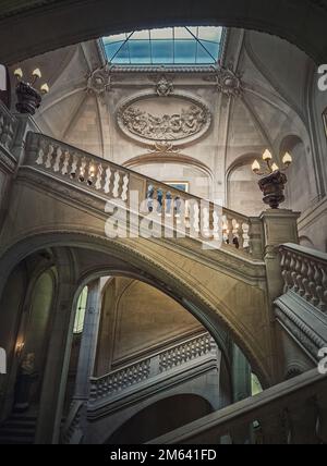 Louvre Palast architektonische Details einer Halle mit Steintreppe, kunstvoll verzierten Geländern und glühenden alten Lampen, Paris, Frankreich Stockfoto