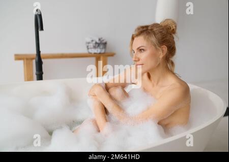 Junge Frau, die im Badezimmer mit Schaumstoffblasen badet Stockfoto