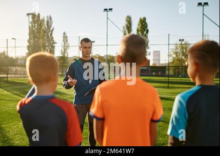 Junger Fußballtrainer, der Kindern auf dem Fußballfeld beibringt Stockfoto