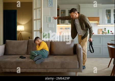 Vater mit Ledergürtel schreit auf Sohn, der Computervideospiele spielt Stockfoto