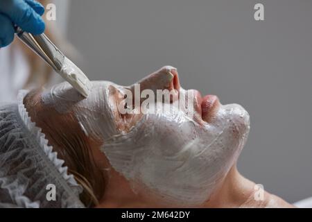Auftragen einer Tonmaske auf das Gesicht einer Mandantin Stockfoto