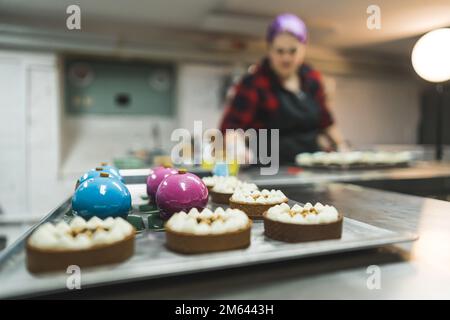 Professionelles Bäckereikonzept. Dekorative Cupcakes Mit Weiblicher Bäckerin. Im Hintergrund verschwommen. Schöne Mini-Törtchen im Vordergrund. Hochwertiges Foto Stockfoto