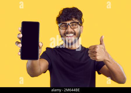 Glücklicher zufriedener Inder empfiehlt eine neue mobile Anwendung oder Website auf orangefarbenem Hintergrund. Stockfoto