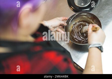 Konditorin in Arbeit. Kleinunternehmer. Ein Foto aus einem großen Winkel, bei dem eine Person Schokoladenteig mit einem Teigschaber mischt. Hochwertiges Foto Stockfoto