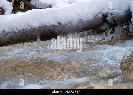 Tiefkühleis-Fluss-Nahaufnahme. Der schnelle Fluss des kalten reinsten Bergflusses stürzt über die Steine. Das Konzept von Winter, kaltem Wetter und Frühling Stockfoto