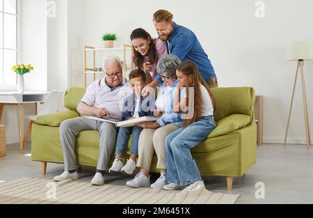 Große Familieneltern, Kinder, Großeltern, die ein Familienfoto suchen, sitzen zusammen im Wohnzimmer. Stockfoto