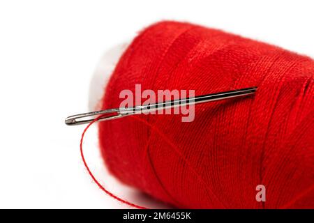 Nadelauge mit rotem Polyesterfaden. Spule aus rotem Polyester-Nähfaden im Hintergrund. Selektiver Fokus. Bokeh. Stockfoto