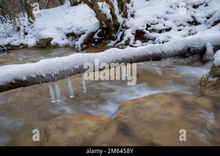 Tiefkühleis-Fluss-Nahaufnahme. Der schnelle Fluss des kalten reinsten Bergflusses stürzt über die Steine. Das Konzept von Winter, kaltem Wetter und Frühling Stockfoto