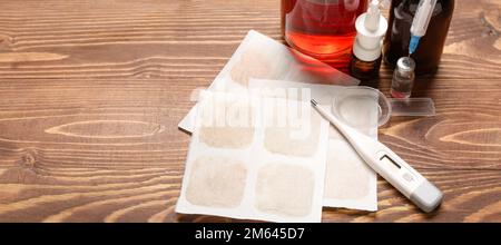 Senfpflaster mit Medikamenten, Tasse Tee und Thermometer auf Holzhintergrund mit Platz für Text Stockfoto