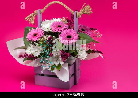 Wunderschöner Blumenstrauß im Korb auf pinkfarbenem Hintergrund. Stockfoto