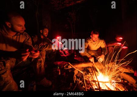 USA Air Force Special Warfare Operators Camp um ein Feuer im Dschungel von Wahiawa, Hawaii, 29. März 2022. Zwischen den Trainingstagen kampierten die 38. Rettungsschwadron Blue Team Sanitäter und ein Joint Terminal Attack Controller, der der 607. Air Support Operations Group zugeteilt war, im Dschungel, um sich mit der Umgebung vertraut zu machen. Der Hauptzweck des Kampftrainings im Dschungel war die Anpassung von Rettungstaktiken, -Techniken und -Verfahren für die Region Indo-Pazifik. Stockfoto