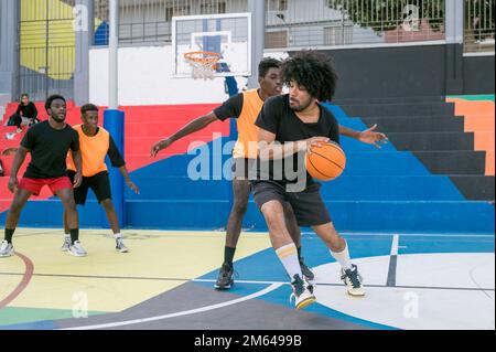 Multiethnische Freunde spielen Basketball auf Sportplatz Stockfoto