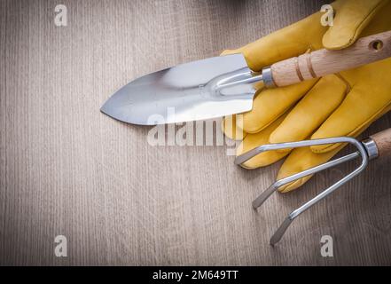 Rostfreier Handspatenrechen gelbes Leder Gartenhandschuhe auf Holzbrettern Landwirtschaftskonzept. Stockfoto