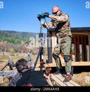 Männliche Arbeiter bauen Pfahlfundament für Holzrahmenhaus. Männer Bauherren Bohren Stapel in den Boden auf blauem Himmel Hintergrund. Stockfoto