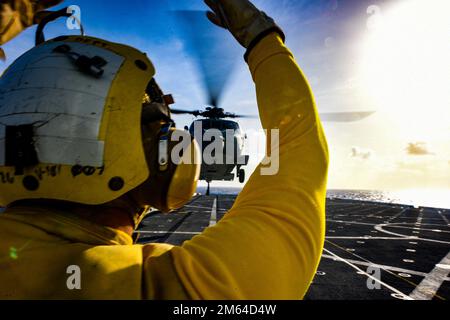 PACIFIC OCEAN (31. März 2022) Aviation Boatswain’s Mate 3. Class Jonathan Patito aus Los Angeles, dem Amphibienschiff USS John P. Murtha (LPD 26) zugewiesen, weist einen MH-60s Sea Hawk Helikopter, der an den „Inselrittern“ der Helicopter Sea Combat Squadron (HSC) 25 befestigt ist, an, an, während der Flugquartiere aufzusteigen; März 31. John P. Murtha führt gerade Routineeinsätze in der US-7.-Flotte durch. Stockfoto