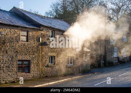 Limbrick, Lancashire. Wetter in Großbritannien. -3 °C im Nordwesten, da die frühe Morgensonne die Wärmedampfemissionen von Wohngrundstücken in Long Lane deutlich macht. Kessel erzeugen lange Dampffahnen, wobei die Luftfeuchtigkeit ebenfalls eine wichtige Rolle bei den Kondensationsprozessen spielt. Rauchgase kommen in Kontakt mit der kalten, feuchten Luft und beginnen dann mit der Erzeugung langer Wasserfahnen winziger Wassertropfen. Kredit: MediaWorldImages/AlamyLiveNews Stockfoto