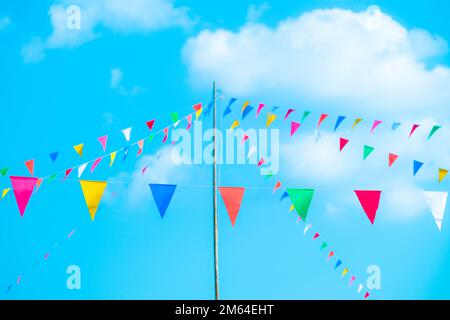 Bunte kleine Flaggen am Himmel. Winkende kleine bunte Flaggen, die am Seil hängen, um Urlaub vor blauem Himmel zu machen. Stockfoto