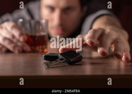 Nicht trinken und Auto fahren. Betrunkener Mann mit Glasalkohol in der Hand, der Autoschlüssel nimmt. Stockfoto