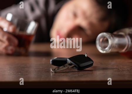 Nicht trinken und Auto fahren. Betrunkener Mann mit Glasalkohol in der Hand sieht auf Autoschlüssel. Stockfoto