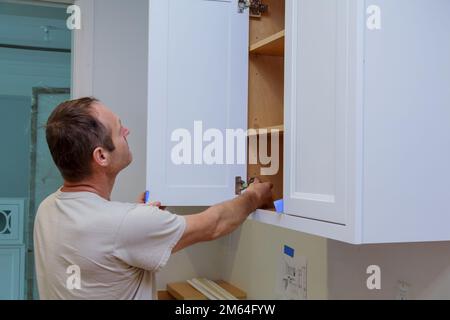 Zimmermannsarbeiter, der die Tür zum Küchenschrank im neuen Heim repariert Stockfoto